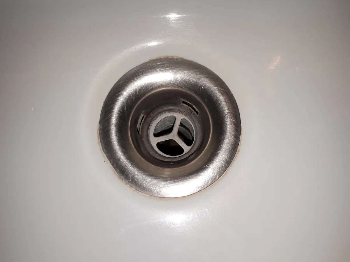 Desagüe metálico de un lavabo blanco de baño, con su rejilla en forma de cruz